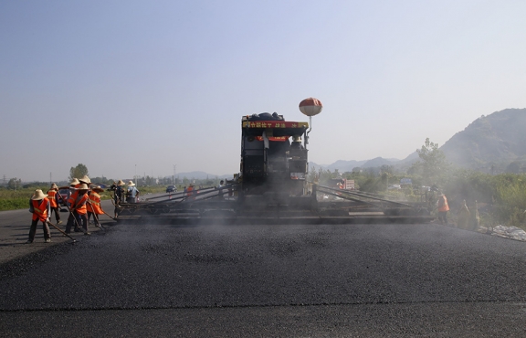 2019年8月，宜春經(jīng)開區(qū)S311路面攤鋪現(xiàn)場(chǎng)，工友們輔助路面兩側(cè)的分料、補(bǔ)窩等作業(yè)